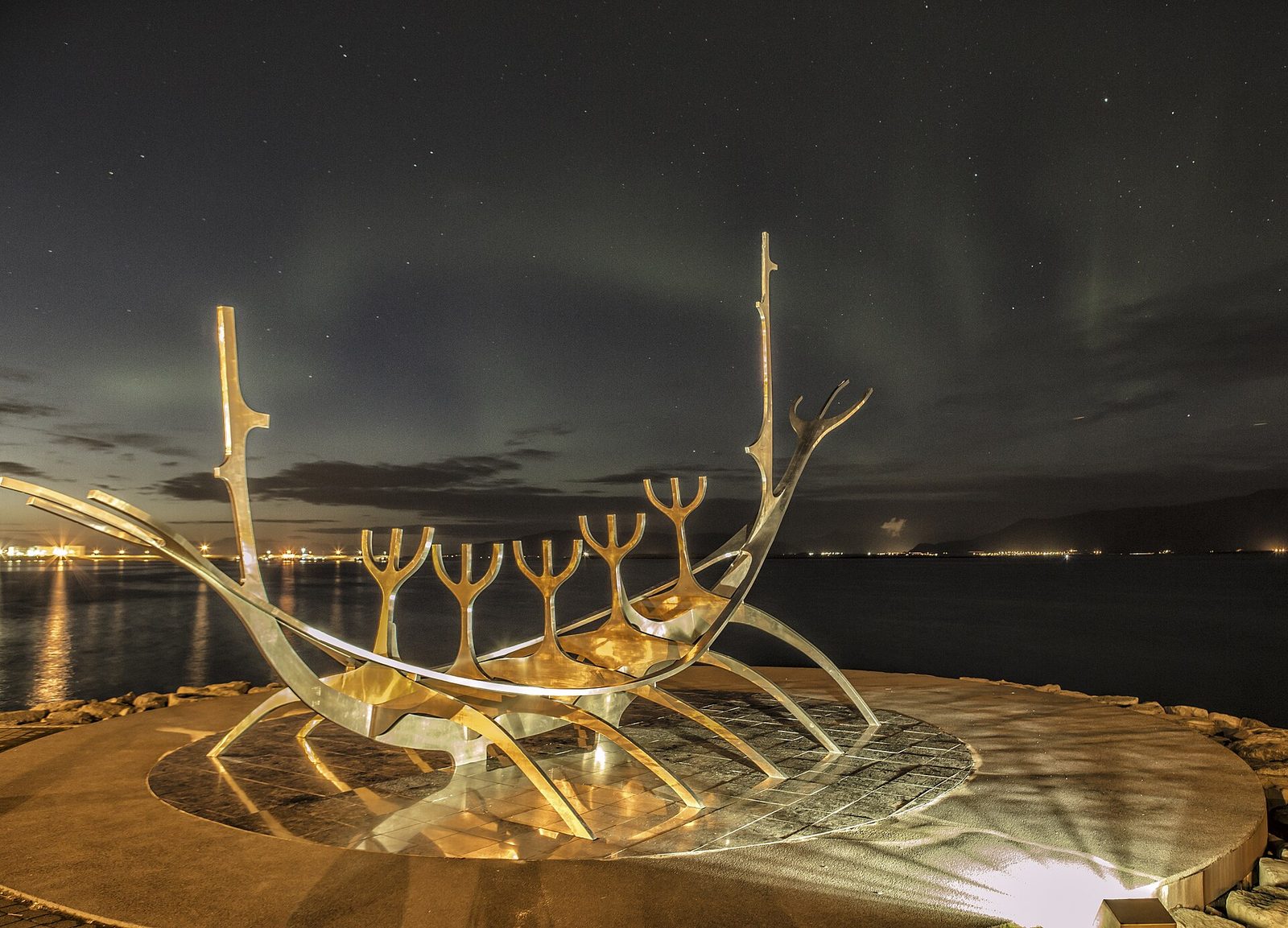 A green aurora over the Sun Voyager steel sculpture on the Reykjavík waterfront, with city lights along the shore, photographed on 19 September 2017