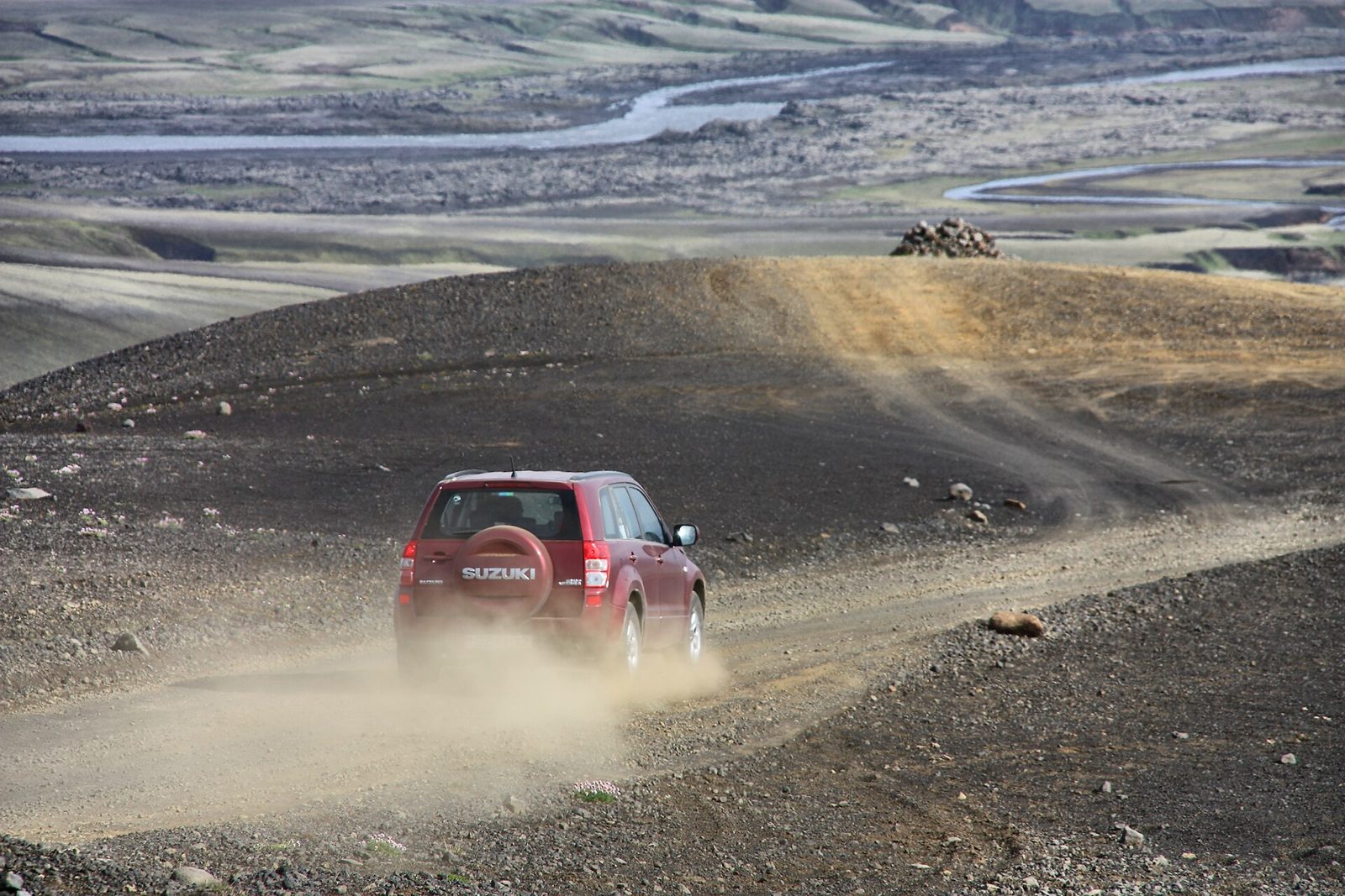 A red 4x4 throwing up dust and gravel on an unpaved highland road in South Iceland